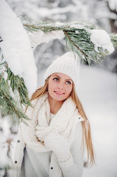 Portrait of a woman in white clothes in a cold winter forest. A girl with a white hat on her head in a snow-covered winter forest.