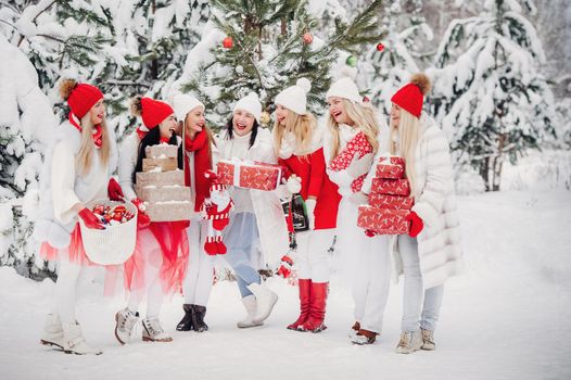 A large group of girls with Christmas gifts in their hands standing in the winter forest.Girls in red and white clothes with Christmas gifts in the snowy forest.