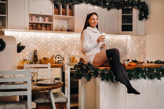 A girl on Christmas day is sitting on the kitchen table and holding a glass of champagne.Woman on new year's eve with champagne.