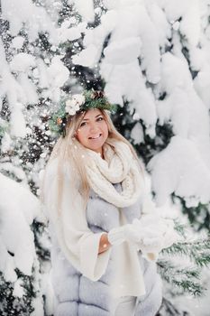 Portrait of a woman in a white fur coat in a cold winter forest. Girl with a wreath on her head in a snow-covered winter forest.