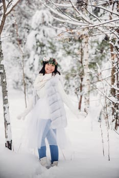 Portrait of a woman in white clothes in a cold winter forest. Girl with a wreath on her head in a snow-covered winter forest