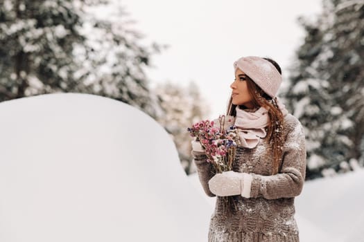 A girl in a sweater in winter with a bouquet in her hands stands among large snowdrifts.