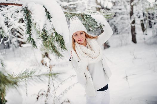 Portrait of a woman in white clothes in a cold winter forest. A girl with a white hat on her head in a snow-covered winter forest.