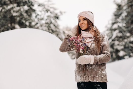 A girl in a sweater in winter with a bouquet in her hands stands among large snowdrifts.