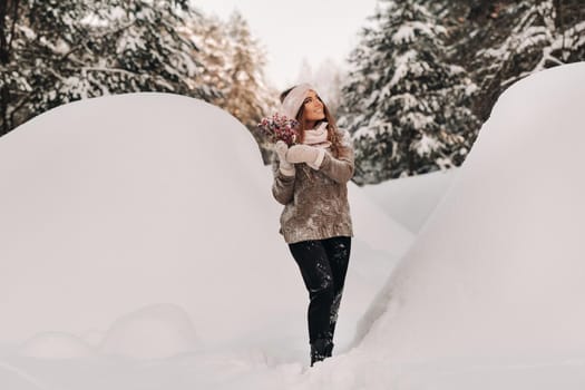 A girl in a sweater in winter with a bouquet in her hands stands among large snowdrifts.