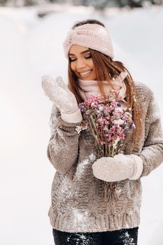 A girl in a sweater in winter with a bouquet in her hands stands among large snowdrifts.