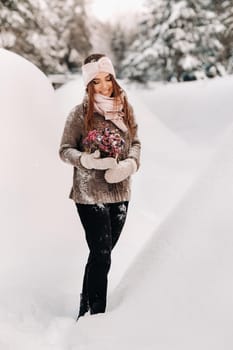 A girl in a sweater in winter with a bouquet in her hands stands among large snowdrifts.