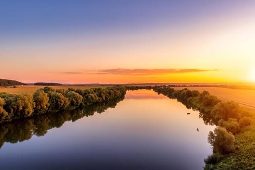 A sunset or sunrise scene over a lake or river with skies reflecting in the water on a summer evening or morning. Landscape.