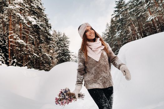 A girl in a sweater in winter with a bouquet in her hands stands among large snowdrifts.