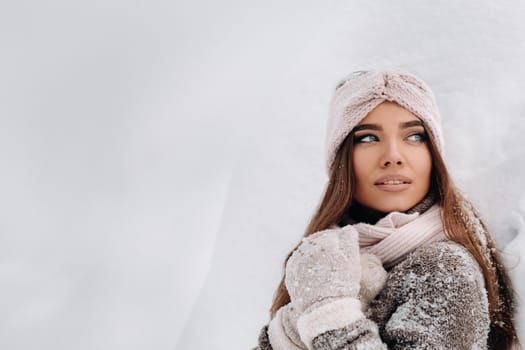 A girl in a sweater and mittens in winter stands on a snow-covered background.