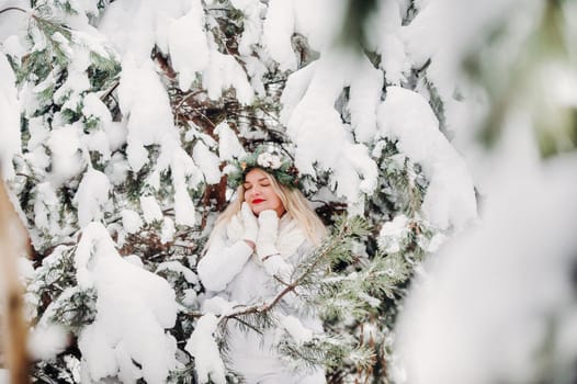 PPortrait of a woman in white clothes in a cold winter forest. Girl with a wreath on her head in a snow-covered winter forest.