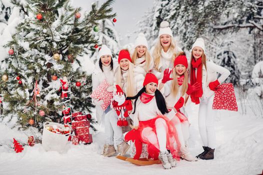 A large group of girls with Christmas gifts in their hands standing in the winter forest.Girls in red and white clothes with Christmas gifts in the snowy forest.