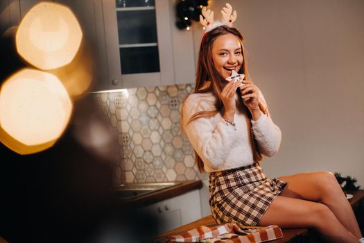 A girl on Christmas day is sitting on the kitchen table and holding cookies in her hands.Woman on new year's eve in the kitchen.