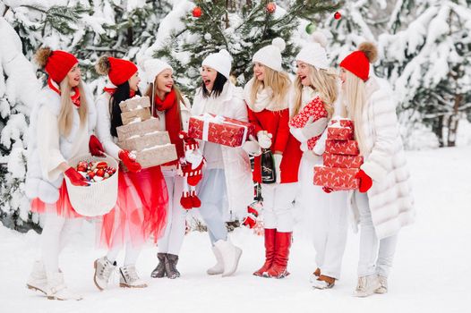 A large group of girls with glasses of champagne in their hands stands in the winter forest.Girls in red and white clothes with new year's drinks in a snow-covered forest