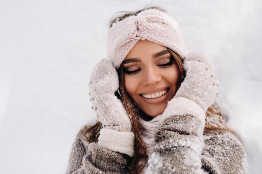 A girl in a sweater and mittens in winter stands on a snow-covered background.