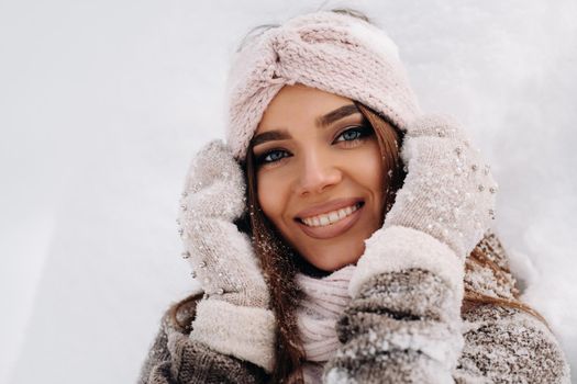 A girl in a sweater and mittens in winter stands on a snow-covered background.