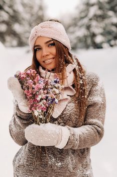 A girl in a sweater in winter with a bouquet in her hands stands among large snowdrifts.