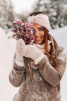 A girl in a sweater in winter with a bouquet in her hands stands among large snowdrifts.