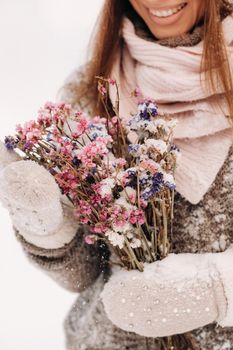 A girl in a sweater in winter with a bouquet in her hands stands among large snowdrifts.