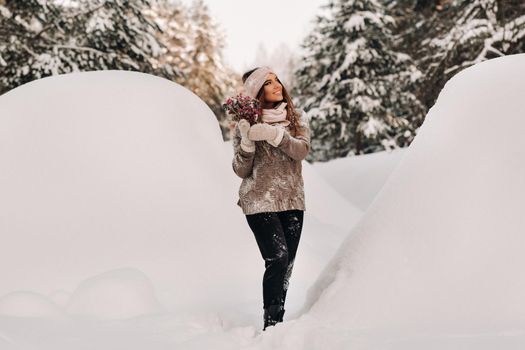 A girl in a sweater in winter with a bouquet in her hands stands among large snowdrifts.