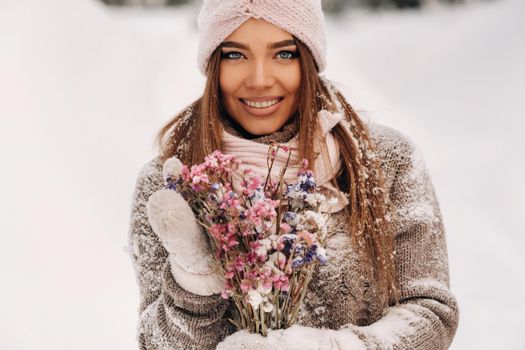 A girl in a sweater in winter with a bouquet in her hands stands among large snowdrifts.