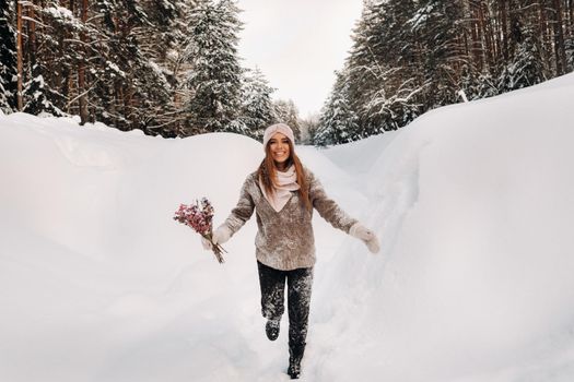 A girl in a sweater in winter with a bouquet in her hands stands among large snowdrifts.