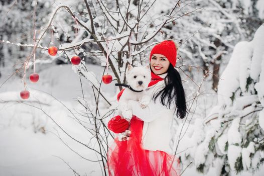 Portrait of a woman in a red jacket with a dog in a cold winter forest. A girl holds a dog in her hands in a snow-covered winter forest.