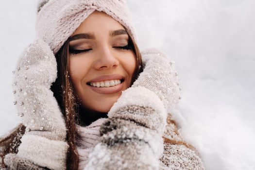 A girl in a sweater and mittens in winter stands on a snow-covered background.