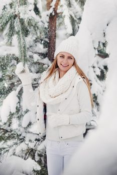 Portrait of a woman in white clothes in a cold winter forest. A girl with a white hat on her head in a snow-covered winter forest.