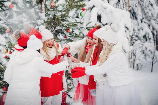 A large group of girls with glasses of champagne in their hands stands in the winter forest.Girls in red and white clothes with new year's drinks in a snow-covered forest