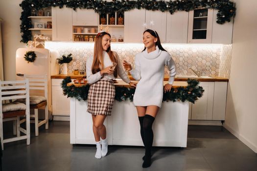 two girls in a cozy home environment with champagne in their hands at Christmas. Smiling girls drink champagne on a festive evening.