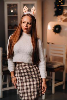 Girl for Christmas with reindeer horns in the home interior.A woman on New year's eve in a white sweater and skirt.