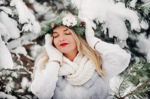 PPortrait of a woman in white clothes in a cold winter forest. Girl with a wreath on her head in a snow-covered winter forest.