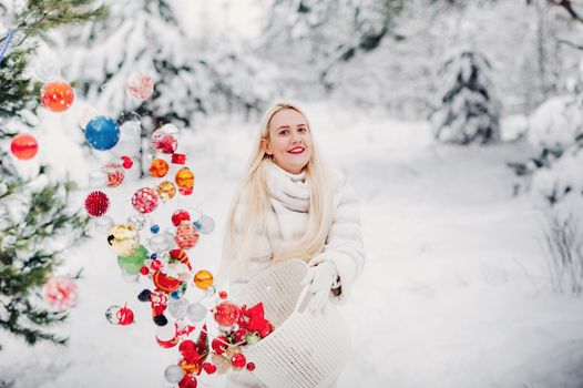A girl in a white jacket throws Christmas balls to decorate the Christmas tree.A girl throws Christmas decorations from a basket into the winter forest.
