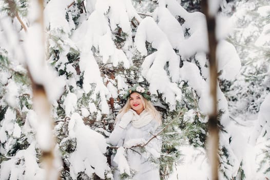 PPortrait of a woman in white clothes in a cold winter forest. Girl with a wreath on her head in a snow-covered winter forest.