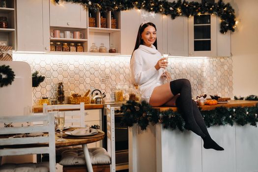 A girl on Christmas day is sitting on the kitchen table and holding a glass of champagne.Woman on new year's eve with champagne.