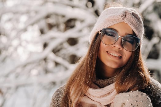 A girl in a sweater and glasses in winter in a snow-covered forest.