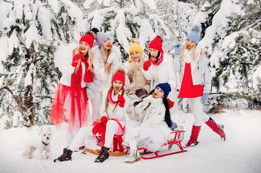 A large group of girls with lollipops in their hands stands in the winter forest.Girls in red and white clothes with candy in a snow-covered forest