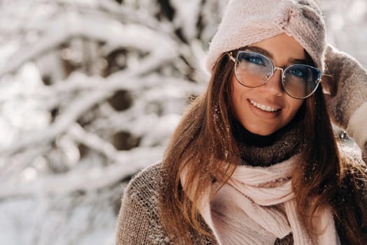 A girl in a sweater and glasses in winter in a snow-covered forest.