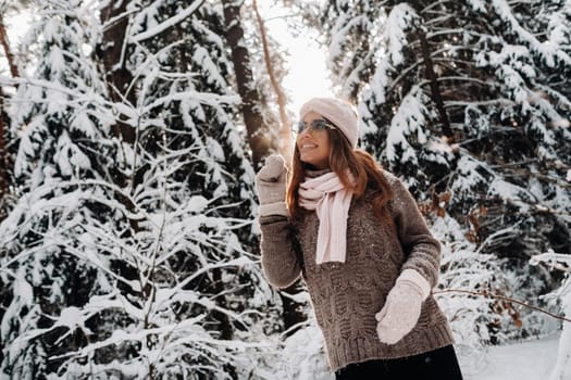 A girl in a sweater and glasses in winter in a snow-covered forest.