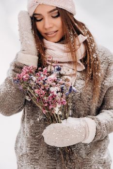 A girl in a sweater in winter with a bouquet in her hands stands among large snowdrifts.