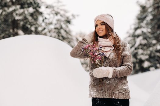 A girl in a sweater in winter with a bouquet in her hands stands among large snowdrifts.
