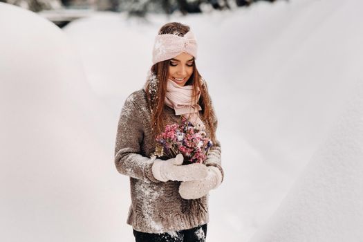 A girl in a sweater in winter with a bouquet in her hands stands among large snowdrifts.