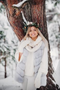 Portrait of a woman in a white fur coat in a cold winter forest. Girl with a wreath on her head in a snow-covered winter forest.