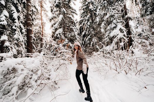 A girl in a sweater and glasses walks in the snow-covered forest in winter.