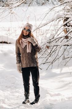 A girl in a sweater and glasses in winter in a snow-covered forest.