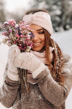 A girl in a sweater in winter with a bouquet in her hands stands among large snowdrifts.