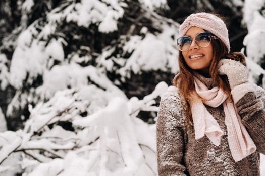 A girl in a sweater and glasses in winter in a snow-covered forest.