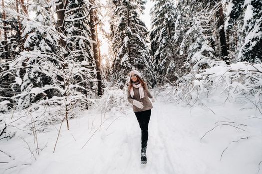 A girl in a sweater and glasses walks in the snow-covered forest in winter.