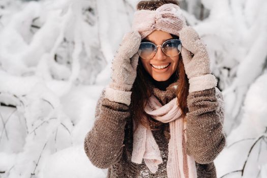 A girl in a sweater and glasses in winter in a snow-covered forest.